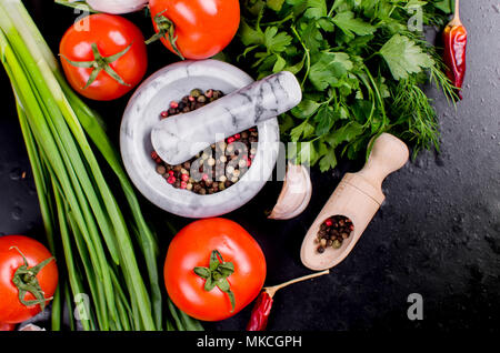 Cherry Tomaten, grüne Zwiebeln und Petersilie, Knoblauch, solt im Löffel und Gewürze auf einem schwarzen Hintergrund Reif. Ansicht von oben, Kopieren. Stockfoto