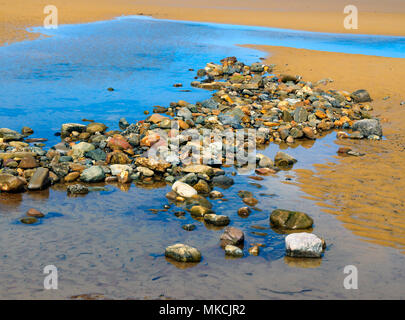 Pool auf einem sandigen Strand bei Ebbe mit Kopfsteinpflaster und kleinen Meer getragen Felsen Stockfoto