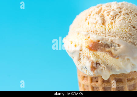 Scoop der Köstlichen Schmelzen gesalzen Karamell Toffee Vanille Eis in der Waffel Kegel auf blauem Hintergrund. Sommer Süßigkeiten Zucker Genuss Konzept Stockfoto