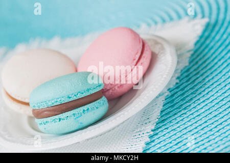 Drei Makronen in verschiedenen Farben und verschiedenen Geschmacksrichtungen in einer weißen Platte, weiß Serviette. Stockfoto