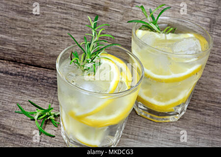Detox Wasser gewürzt mit in Scheiben geschnittenen Zitrone und Rosmarin auf einem rustikalen Holztisch Stockfoto