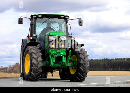 Bauer macht eine Rechtskurve mit John Deere 6150R Traktoren und landwirtschaftliche Anhänger an der Hauptstraße. Jokioinen, Finnland - 30. April 2018. Stockfoto