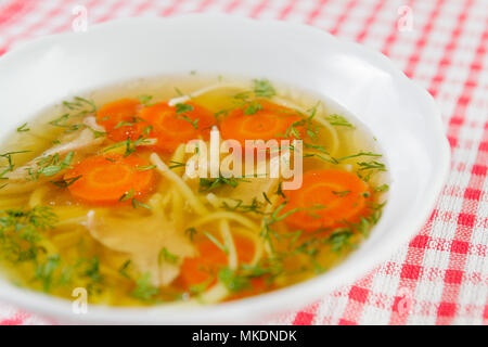 Huhn Suppe oder Brühe mit Nudeln, Hähnchen Fleisch, Karotten Scheiben und Kräutern in weiße Schüssel. Stockfoto