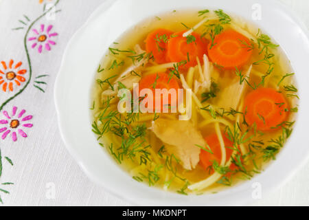 Huhn Suppe oder Brühe mit Nudeln, Hähnchen Fleisch, Karotten Scheiben und Kräutern in weiße Schüssel. Stockfoto