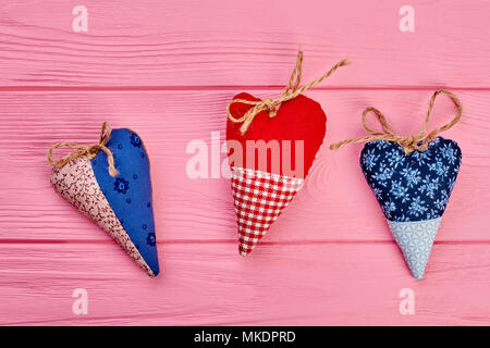 Drei farbenfrohe handgefertigte Herzen. Stoff Herz auf rosa Holz gemusterten Hintergrund. Happy Valentines Tag. Stockfoto