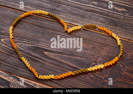 Form des Herzens von ungekochte Teigwaren. Getrocknete Fusilli auf braunem Holz- Hintergrund. Stockfoto