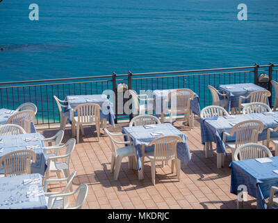 Tische und Stühle von einem Restaurant auf einer Terrasse mit Blick auf das Meer. Stockfoto