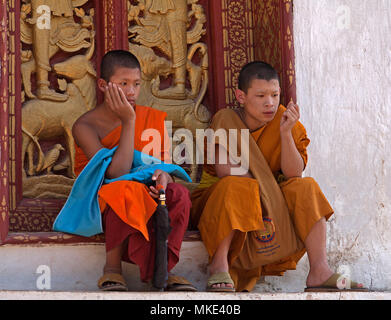 Zwei buddhistische Mönche sitzen auf einem Schritt vor einem moanatery geschnitzte Tür. Stockfoto