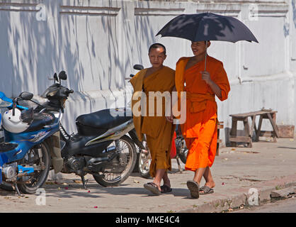 Zwei buddhistische Mönche wandern pass ein Motorrad in Luang Prabang, Laos. Stockfoto