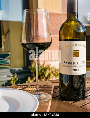 Close up sonnenbeschienenen Rotwein Rotwein Flasche und Glas Wein auf der Terrasse im freien Tisch, Saint-Julien, Grand Vin de Bordeaux Stockfoto