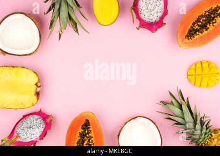 Tropische Früchte Rahmen mit Ananas, Drachenfrucht, Papaya, Kokos und Mango auf einem Pastell rosa Hintergrund Stockfoto