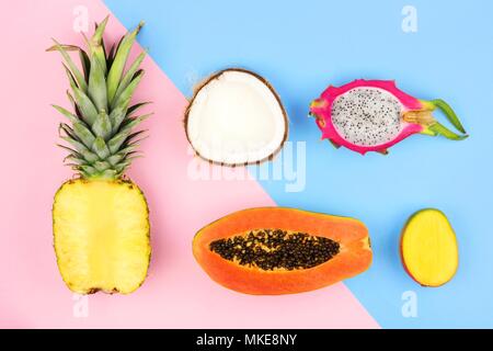 Tropische Früchte flach mit Ananas, Drachenfrucht, Papaya, Mango, und Kokosnuss auf einem Pastell rosa und blauen Hintergrund Stockfoto