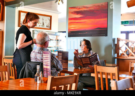 Junge Kellnerin mit einem Essen um von einem Paar mittleren Alters an einem Tisch im Café bei Knott Knott Ende Ende, Wyre, Lancashire, Großbritannien Stockfoto