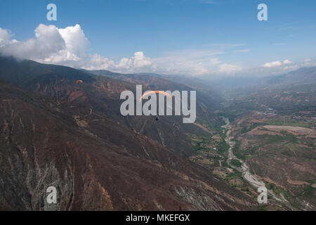 Red Gleitschirme fliegen entlang der Berghang über dem Tal des Flusses unter einem blauen Himmel mit weißen Wolken Cumulus. Stockfoto