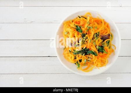 Butternut-kürbis spirilized Nudeln mit Spinat und Kürbiskerne auf weißem Holz Hintergrund, gesunde Ernährung Konzept. Ansicht von oben. Stockfoto