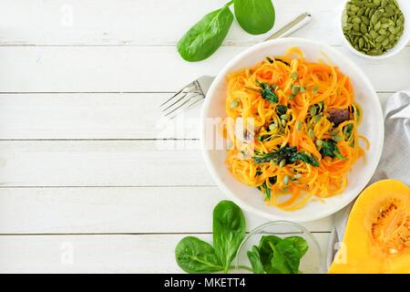 Butternut-kürbis spirilized Nudeln mit Spinat und Kürbiskerne auf weißem Holz Hintergrund, gesunde Ernährung Konzept. Ansicht von oben, seitliche Grenze. Stockfoto