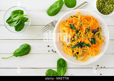 Butternut-kürbis spirilized Nudeln mit Spinat und Kürbiskerne auf weißem Holz Hintergrund, gesunde Ernährung Konzept. Ansicht von oben, Tabelle Szene. Stockfoto