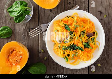 Butternut-kürbis spirilized Nudeln mit Spinat und Kürbiskerne auf dunklen Hintergrund, gesunde Ernährung Konzept. Ansicht von oben, Tabelle Szene. Stockfoto