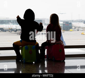 Ein Junge (5 Jahre alt) saß auf seinem Koffer auf die Flugzeuge am Flughafen Heathrow suchen Stockfoto