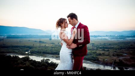 Horizontale halbe Länge Hochzeit Portrait bezaubernd schöne jungvermählte Paar zärtlich umarmen Landschaft Berge Fluß Wald Sonnenuntergang Natur. Stockfoto