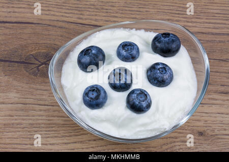 Süße Heidelbeeren in normaler Joghurt. Weißer Joghurt im Glas Schale mit köstlichen Heidelbeeren auf einem vintage Holz- Hintergrund. Stockfoto