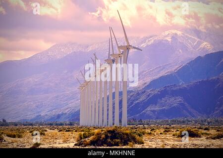 Eine Linie von Windenergieanlagen vor schneebedeckten Bergen auf einem Palm Springs Windpark Stockfoto