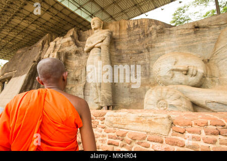 Ein Mönch ist zu Fuß vor der Statue des Liegenden Buddha und Mönch Ananda in das Gesicht von Granitfelsen der Gal Viharaya, Polonnaruwa, Sri Lanka. Stockfoto