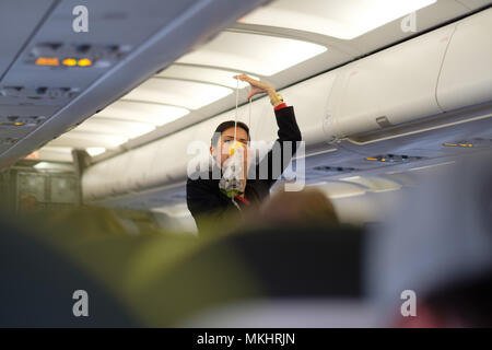 Flug Hostess in Uniform zeigen, wie Sauerstoff Maske des Flugzeuges während Sicherheit Verfahren Demonstration zu verwenden Stockfoto