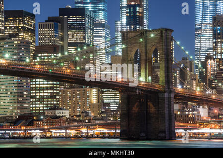 Brooklyn Bridge und die beleuchtete Skyline von Manhattan am Abend mit blauem Himmel und glatte Wasseroberfläche geschossen aus Brooklyn, New York, USA. Stockfoto