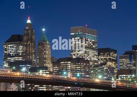 Nahaufnahme, Brooklyn Bridge und die beleuchtete Skyline von Manhattan am Abend mit blauem Himmel und glatte Wasseroberfläche geschossen aus Brooklyn, Neu Stockfoto