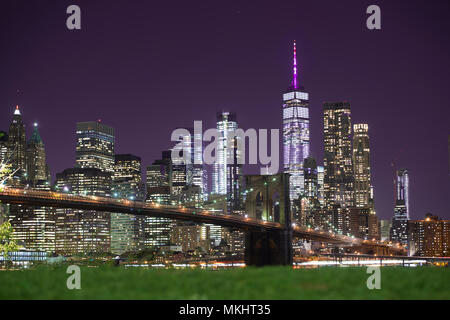 Brooklyn Bridge und die beleuchtete Skyline von Manhattan am Abend mit blauem Himmel und glatte Wasseroberfläche geschossen aus Brooklyn, New York, USA. Stockfoto