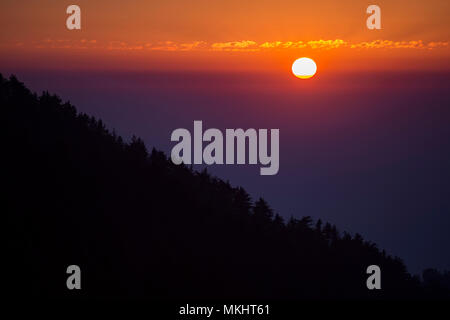 Sonnenuntergang hinter einem Berg mit der Silhouette von Bäumen, in Dharamsala, Indien. Stockfoto