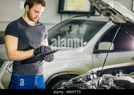 Mechaniker vor einem offenen Wagen Haube mit Zwischenablage und Stift Stockfoto