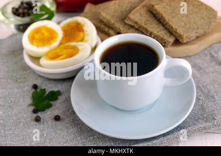 Eine Tasse starken Kaffee (Espresso), close-up und einfache Diät Frühstück - gekochtes Ei und Roggenbrot - im Hintergrund. Stockfoto