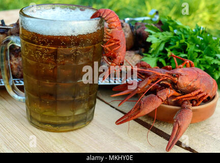 Schäumendem Bier im Glas und gekochte Languste closeup, gegrilltes Fleisch am Spieß im Hintergrund. Für die Feiertage, im Freien genießen. Stockfoto