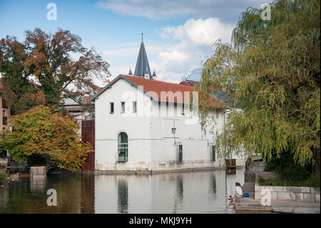 Fluss Thiou, Waterside Bauen & spire von Notre-Dame de Liesse, mit jungen Paar im Vordergrund sitzt. Ruhigen herbst Szene in Annecy, Frankreich Stockfoto