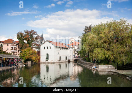 Fluss Thiou, Waterside Bauen & spire von Notre-Dame de Liesse, mit jungen Paar im Vordergrund sitzt. Ruhigen herbst Szene in Annecy, Frankreich Stockfoto