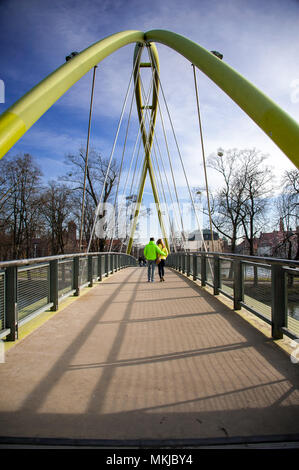 Ein junges Paar gehen Arm in Arm über das Malz Fußgängerbrücke (Kladka Slodowa). Winter scene, symmetrisches Bild, gelb lackiert, gewölbte Brücke, blauer Himmel Stockfoto