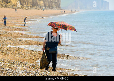 West Bay, Dorset, Großbritannien. 8. Mai 2018. UK Wetter. Eine Frau, die selbst den Schutz von der warmen Frühlingssonne am Strand am Strand von West Bay in Dorset. Der Strand ist heute ruhig nach der Bank Holiday Wochenende wo Sunseeker strömten an die Küste in die Tausende, die die meisten der rekordverdächtigen frühen Bank Holiday Temperaturen Foto: Graham Jagd-/Alamy Leben Nachrichten zu machen Stockfoto