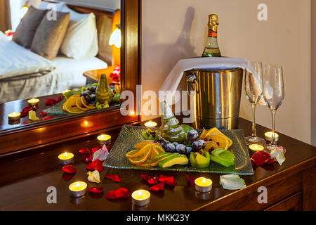 Romantisches Abendessen für Liebhaber: Tabelle mit einer Frucht Teller, Gläser Champagner, Sekt mit Eis in einer Metall Eimer und Kerzen, im Hintergrund ein. Stockfoto