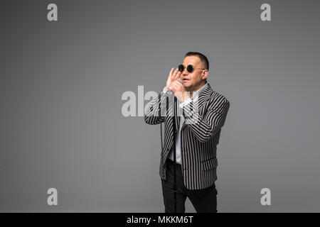 Das mittlere Alter Showman Interviewer mit Emotionen. Junge elegante reifer Mann mit Mikrofon gegen den weißen Hintergrund. Stockfoto