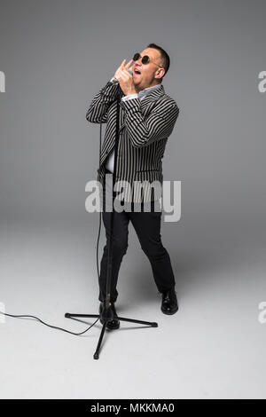 Das mittlere Alter Showman Interviewer mit Emotionen. Junge elegante reifer Mann mit Mikrofon gegen den weißen Hintergrund. Stockfoto