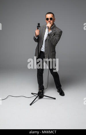Das mittlere Alter Showman Interviewer mit Emotionen. Junge elegante reifer Mann mit Mikrofon gegen den weißen Hintergrund. Stockfoto