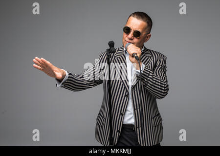 Das mittlere Alter Showman Interviewer mit Emotionen. Junge elegante reifer Mann mit Mikrofon gegen den weißen Hintergrund. Stockfoto