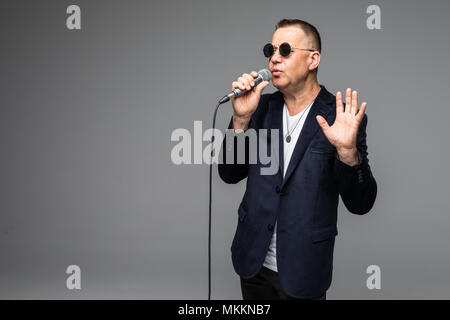 Das mittlere Alter Showman Interviewer mit Emotionen. Junge elegante reifer Mann mit Mikrofon gegen den weißen Hintergrund. Stockfoto