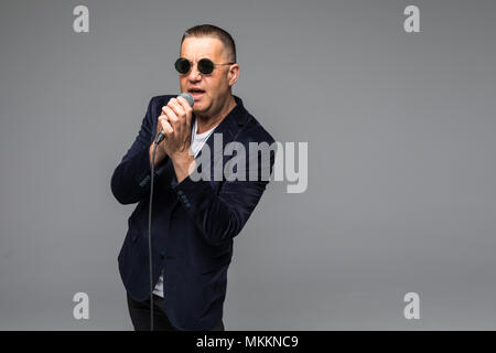 Das mittlere Alter Showman Interviewer mit Emotionen. Junge elegante reifer Mann mit Mikrofon gegen den weißen Hintergrund. Stockfoto