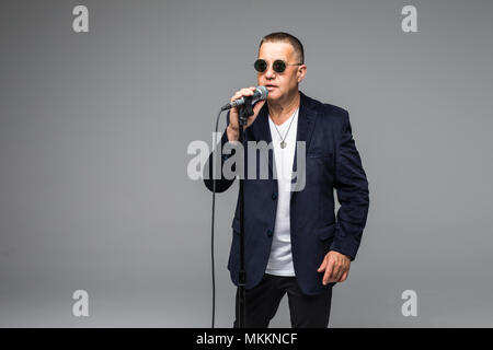 Das mittlere Alter Showman Interviewer mit Emotionen. Junge elegante reifer Mann mit Mikrofon gegen den weißen Hintergrund. Stockfoto