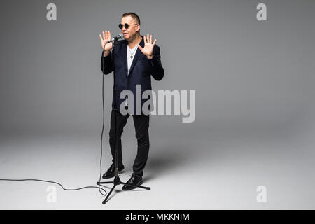 Das mittlere Alter Showman Interviewer mit Emotionen. Junge elegante reifer Mann mit Mikrofon gegen den weißen Hintergrund. Stockfoto