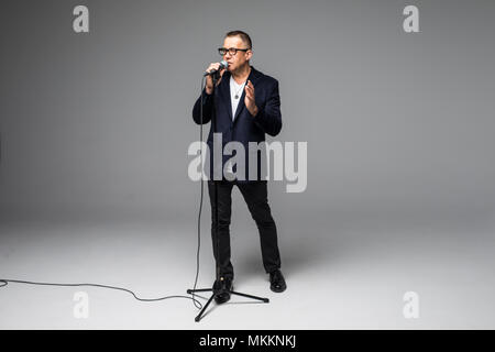Das mittlere Alter Showman Interviewer mit Emotionen. Junge elegante reifer Mann mit Mikrofon gegen den weißen Hintergrund. Stockfoto