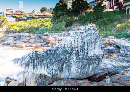 Ein verwitterter Fels am Strand unten einige luxuriöse Apartments mit Meerblick entlang der Coogee Beach Walk, New South Wales, Australien. Stockfoto